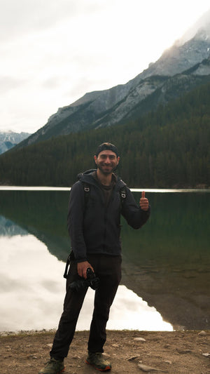 Person giving a thumbs up in front of a mountain lake