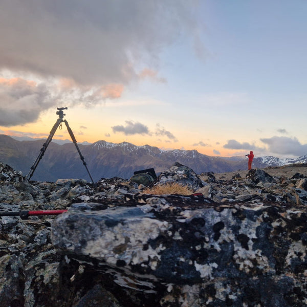 Person with a camera on a tripod in a mountainous landscape during sunset.