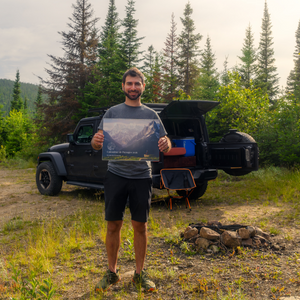 Jamil Slim holding his landscape calendar 2026 in front of a black Jeep in a forest setting