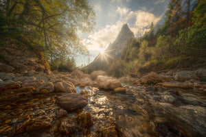 Stream flowing through a rocky landscape with trees and mountains in the background