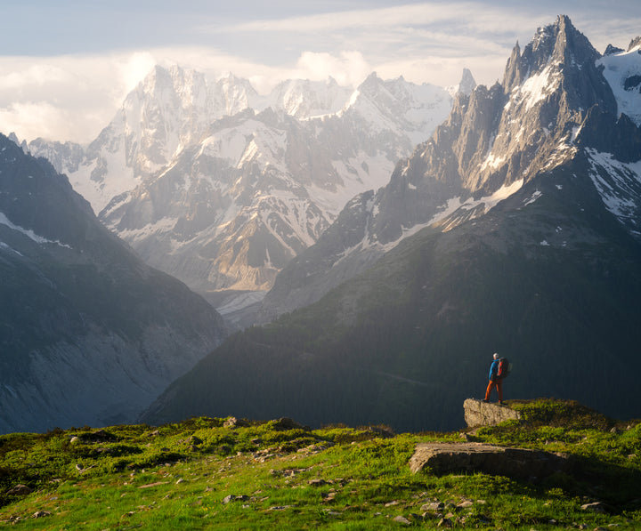 Hiker on a rocky ledge looking at snow-capped peaks and a glacier in the French Alps, landscape photography workshop