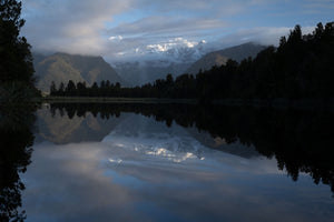 Mountain range reflected in a calm lake with trees on either side.
